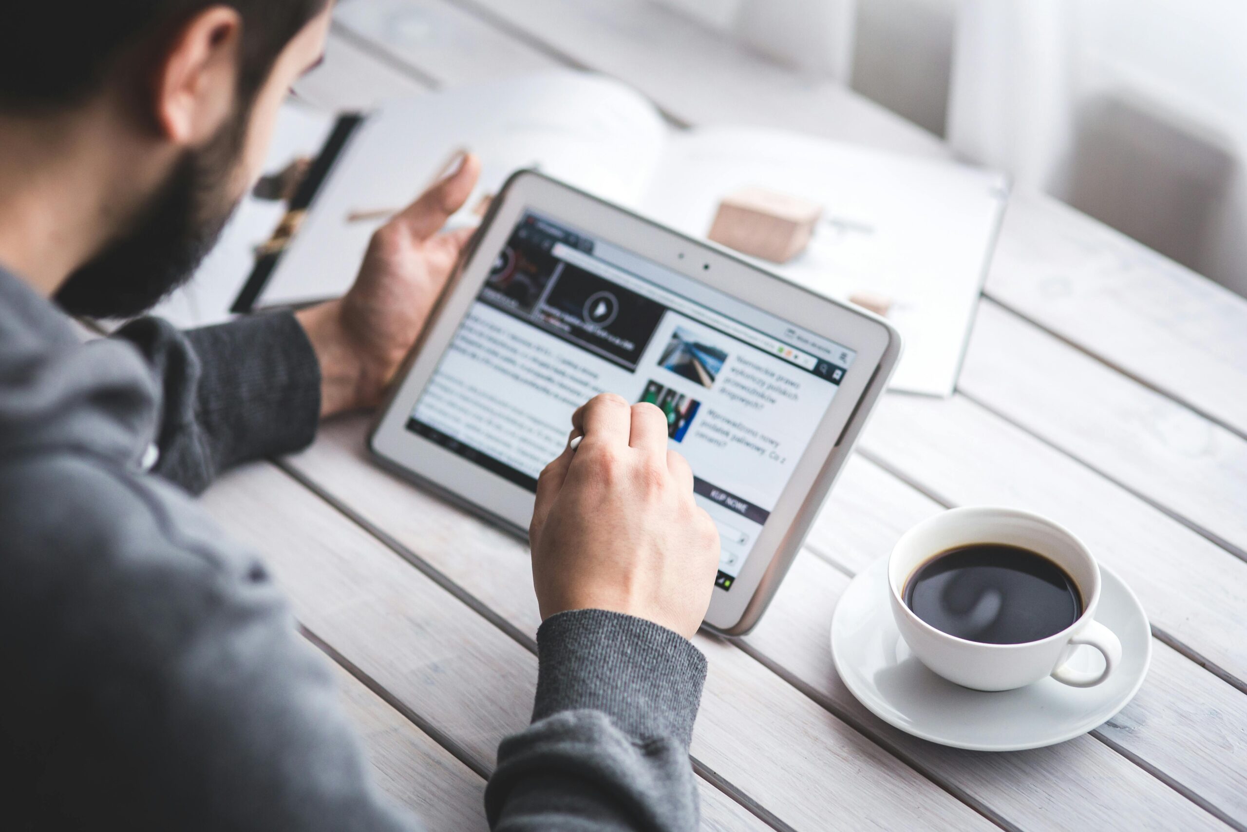 Alcance real: como transformar um simples post em matéria de portal 1 A man uses a tablet to browse news while enjoying a cup of coffee, stylus in hand.